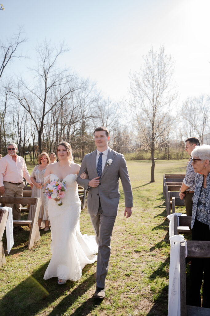 brother wearing grey suit walks bride down the isle outdoor ceremony