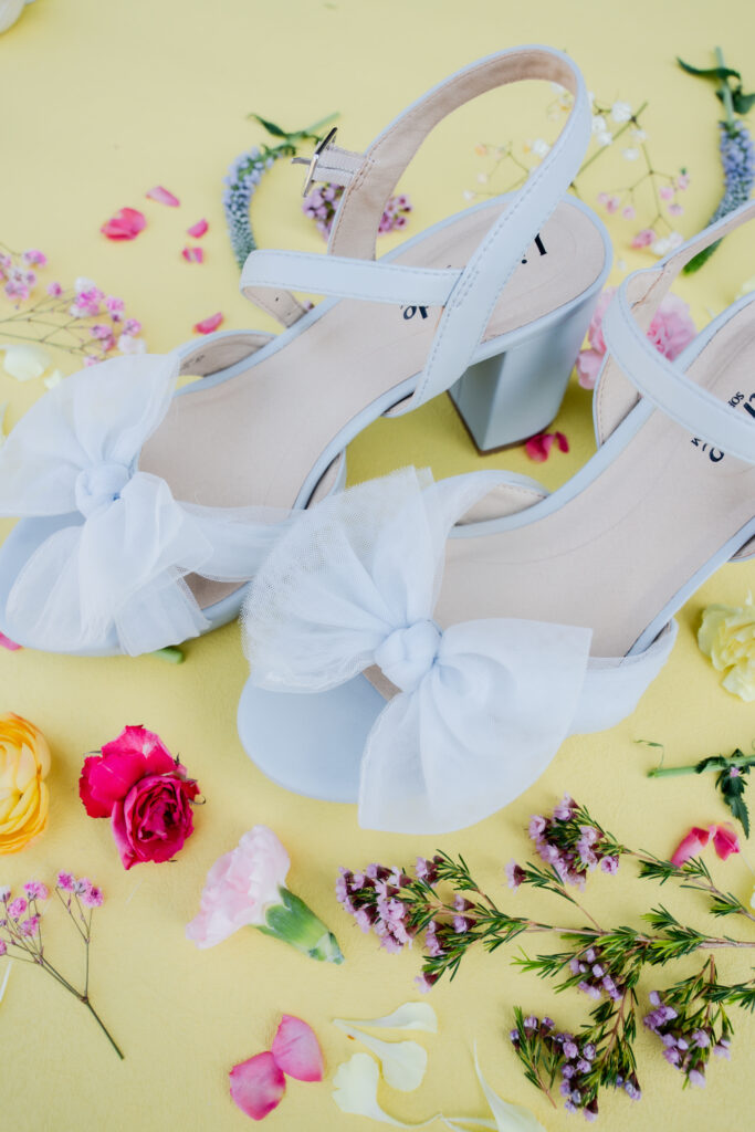 Blue wedding shoes with a bow surrounded by wildflowers on a flat lay mat